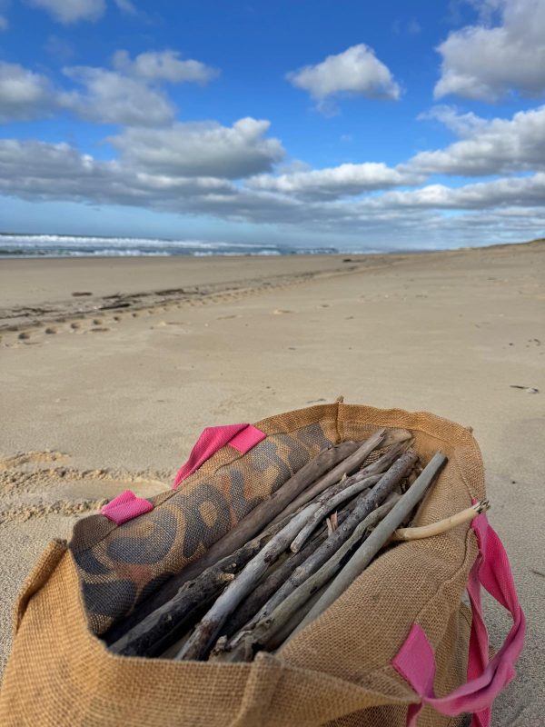 Sac en toile de jute rempli de branches de bois flotté fraîchement ramassées sur le sable, face à l’océan